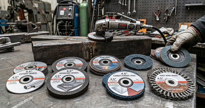 A variety of 4.5-inch angle grinder discs, including flap and knot wire wheels, arranged with a grinder on a bench.