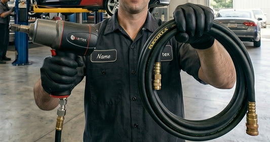 Mechanic in work uniform holding a black air hose and a Kertex impact wrench in a professional automotive garage.