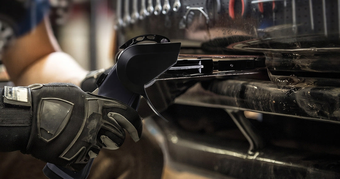 Mechanic using a Le Lematec pneumatic belt sander to clean up a metal weld on an automotive vehicle chassis.